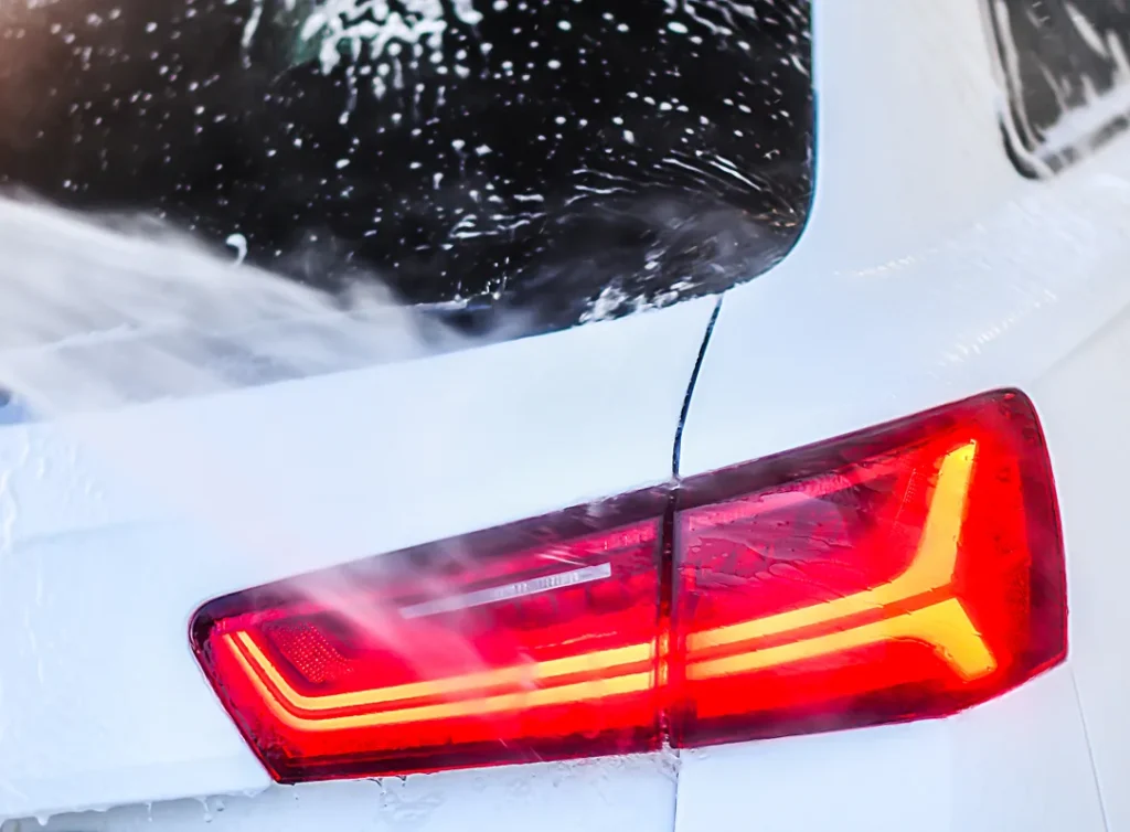 Achterlicht van een witte auto tijdens een wasbeurt bedekt met schuim en water.
